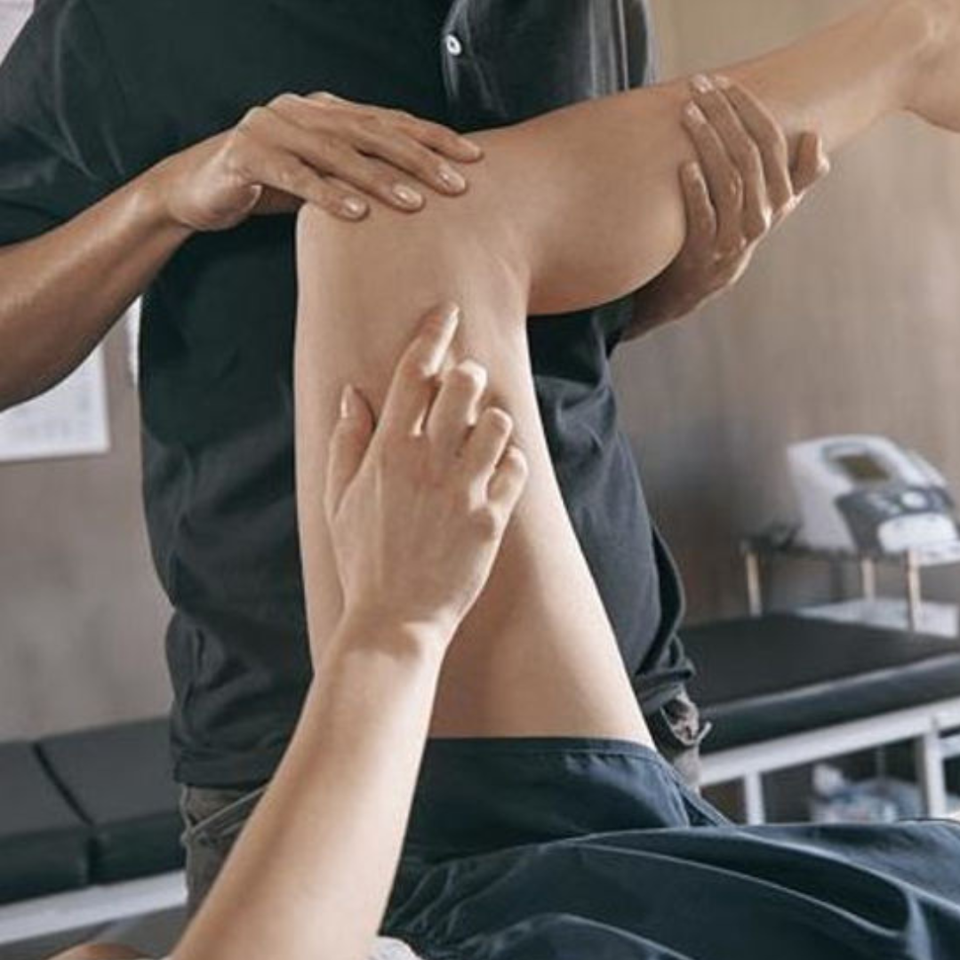 A person is receiving a leg treatment or adjustment from a practitioner, who is holding the leg and applying gentle pressure. The setting appears to be a clinic or therapy room.