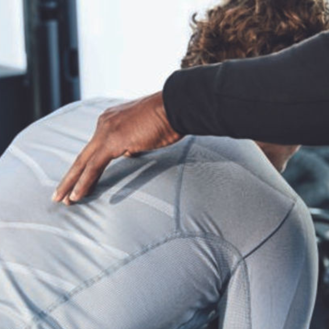 A person is receiving a treatment or adjustment to their back, with a practitioner applying pressure to the shoulder area. The image focuses on the hand of the practitioner and the person’s back.